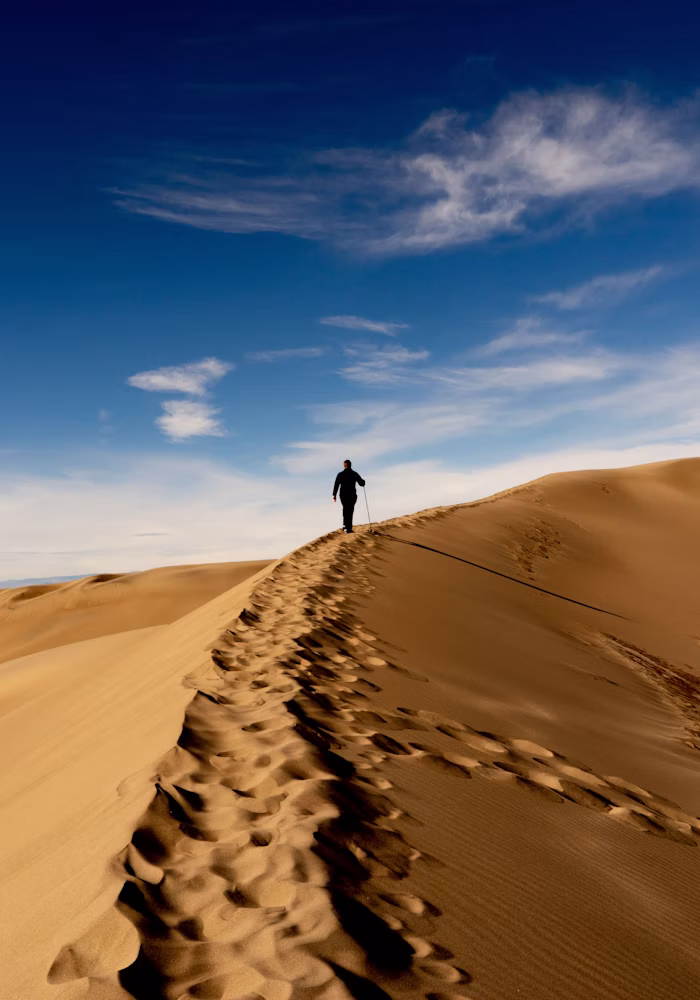 Person wandert allein über eine Sanddüne Richtung Horizont