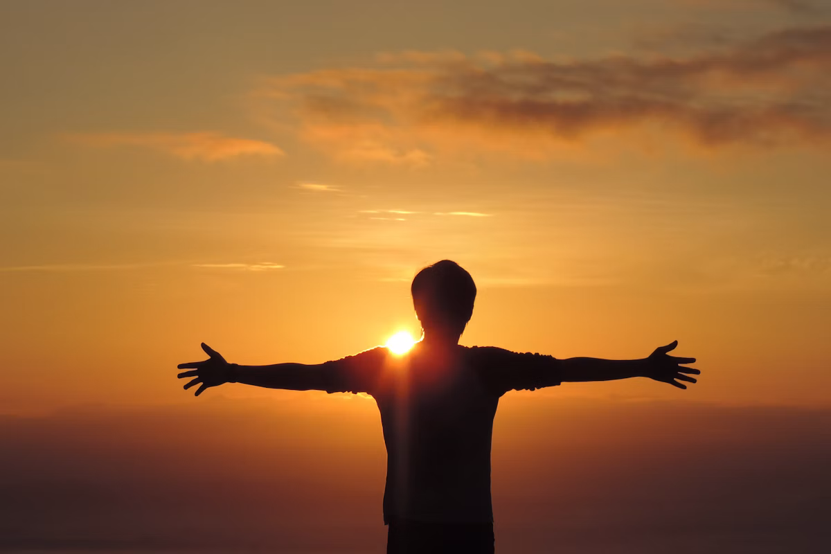 Silhouette einer Person mit ausgebreiteten Armen vor dem Sonnenuntergang